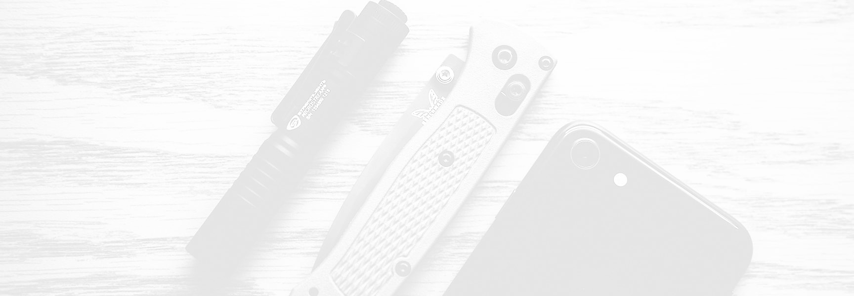 Flashlight, knife, and phone on white wood